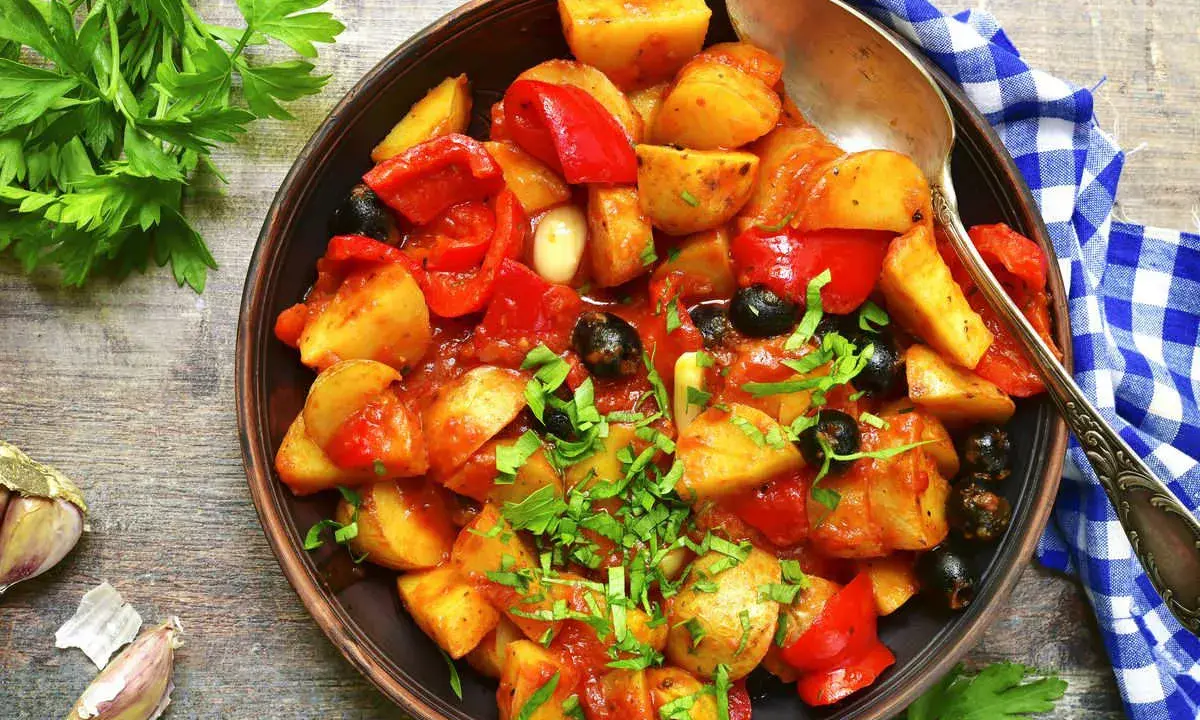 Patate e peperoni in padella, un piatto saporito con olive nere e prezzemolo fresco.