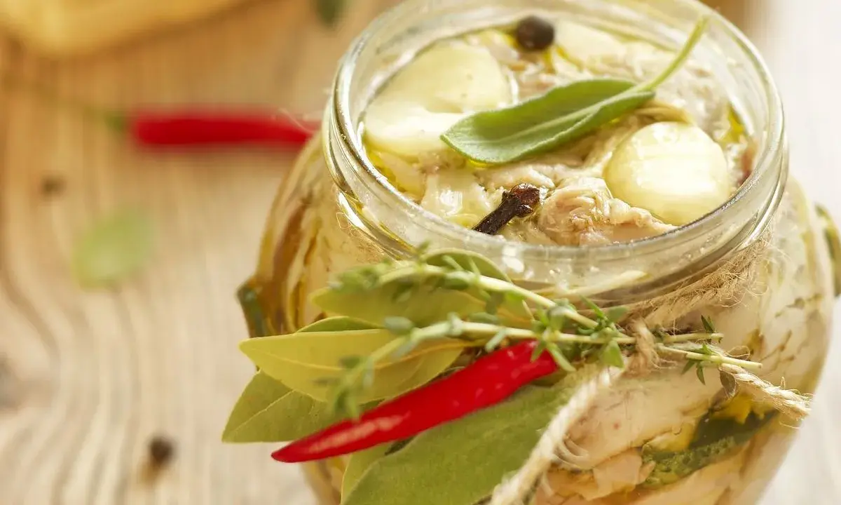 Tonno di coniglio in olio, con erbe aromatiche, peperoncino e spezie, in un barattolo di vetro decorato con spago.