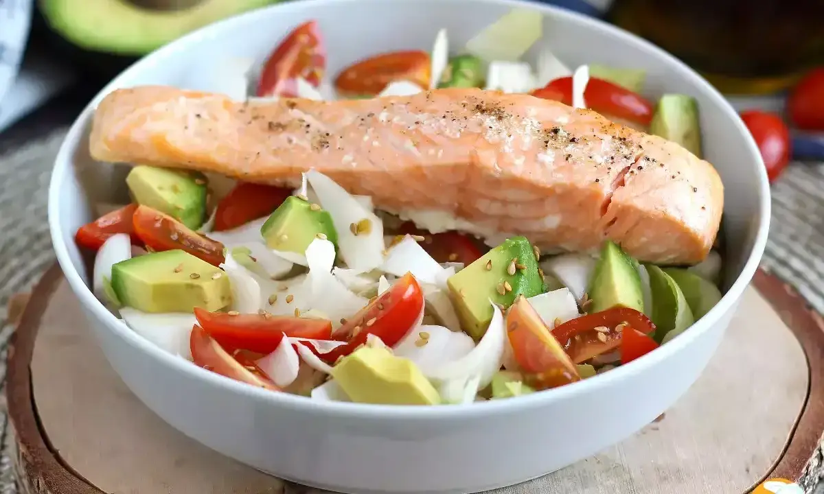 Salmone cotto su un letto di avocado, pomodorini e cipolla bianca, un piatto leggero e gustoso, perfetto come secondi di pesce.