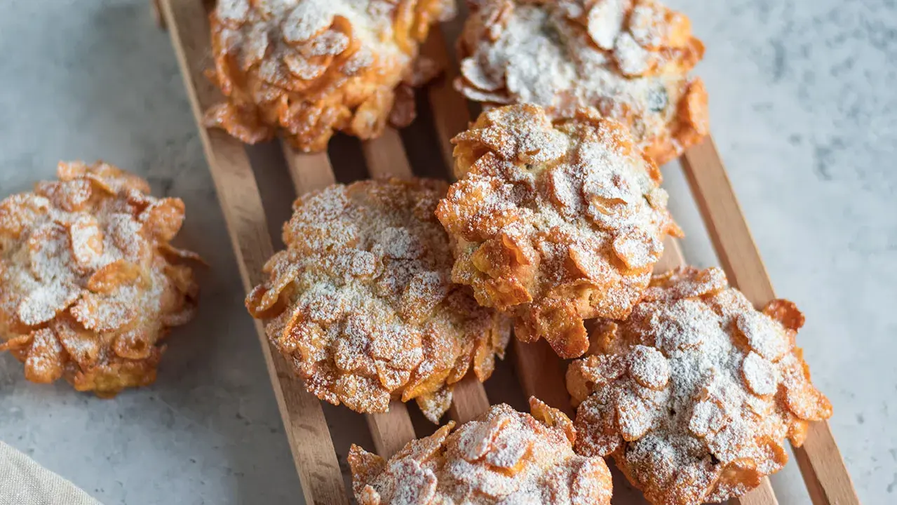 Deliziose rose del deserto, dolcetti croccanti ricoperti di fiocchi di mais e spolverati di zucchero a velo, su un tagliere di legno.