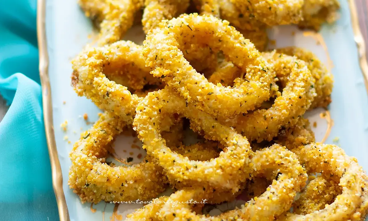 Anelli di totano al forno dorati e croccanti, serviti su un piatto azzurro con un tovagliolo turchese.