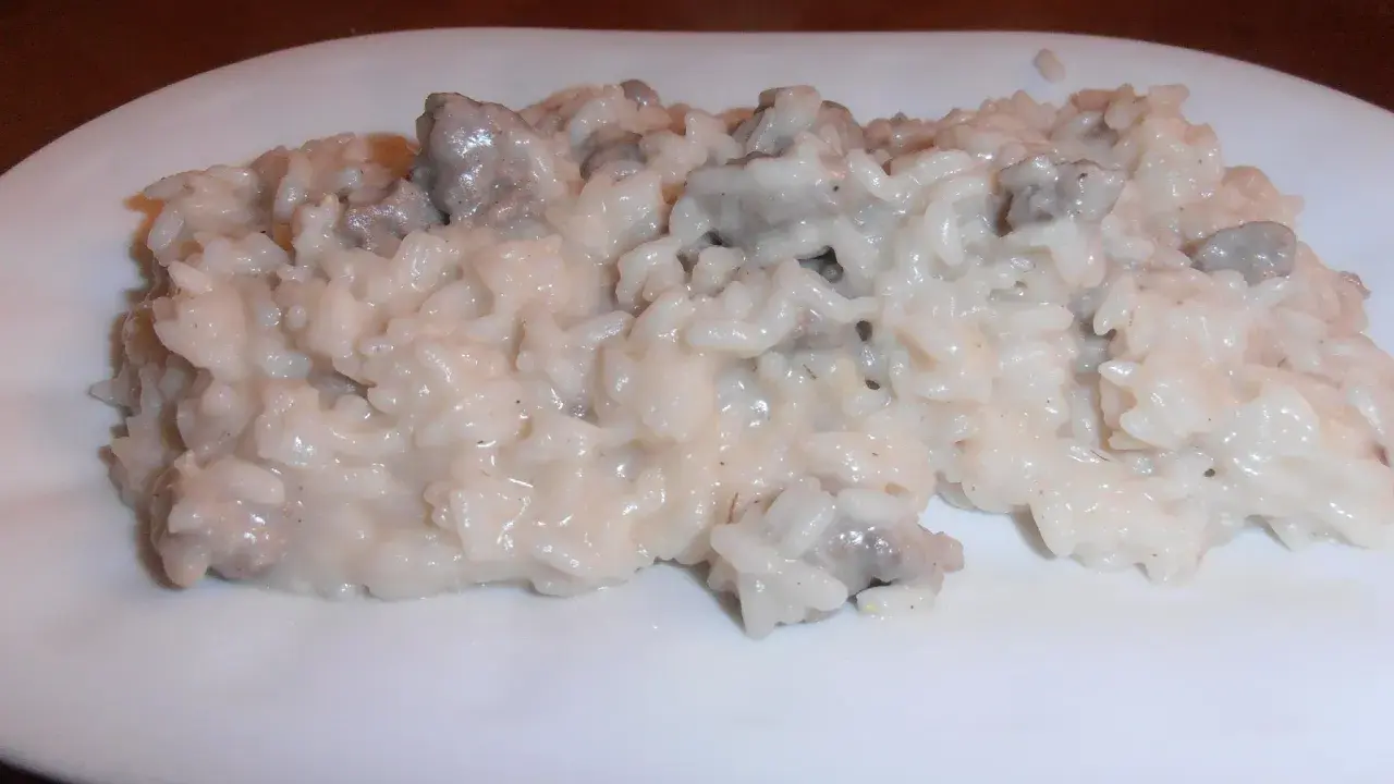 Un cremoso risotto con salsiccia, servito su un piatto bianco.