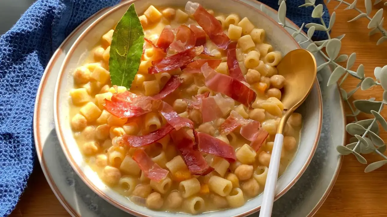 Un piatto fumante di pasta e ceci, guarnito con prosciutto crudo e una foglia di alloro.