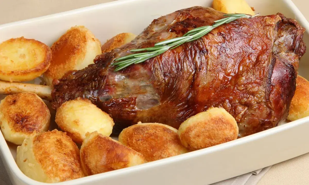 Un succulento agnello al forno con patate arrosto dorate, guarnito con un rametto di rosmarino fresco.