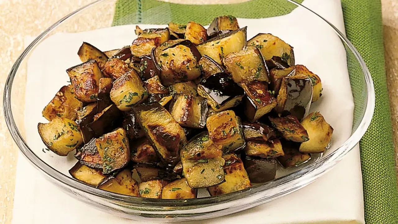 Melanzane a funghetto dorate e saporite, condite con erbe aromatiche, servite in una ciotola di vetro.