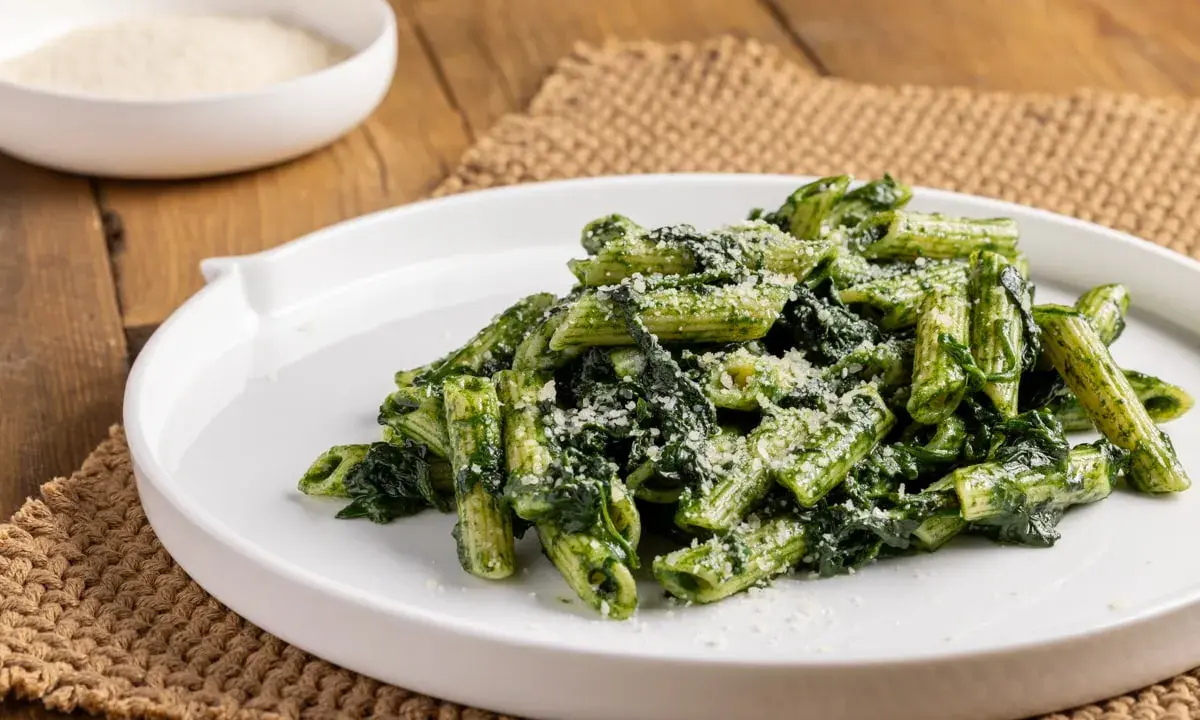 Piatto di pasta con spinaci e parmigiano grattugiato, servito su un piatto bianco.
