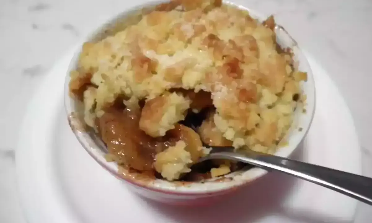 Un delizioso crumble di mele appena sfornato, con la sua crosta dorata e il ripieno succoso, pronto per essere gustato con un cucchiaino.