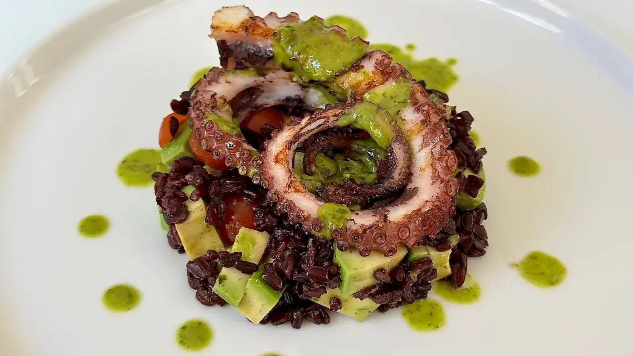 Delizioso polpo alla griglia su letto di riso venere, avocado e pomodorini, condito con salsa verde.