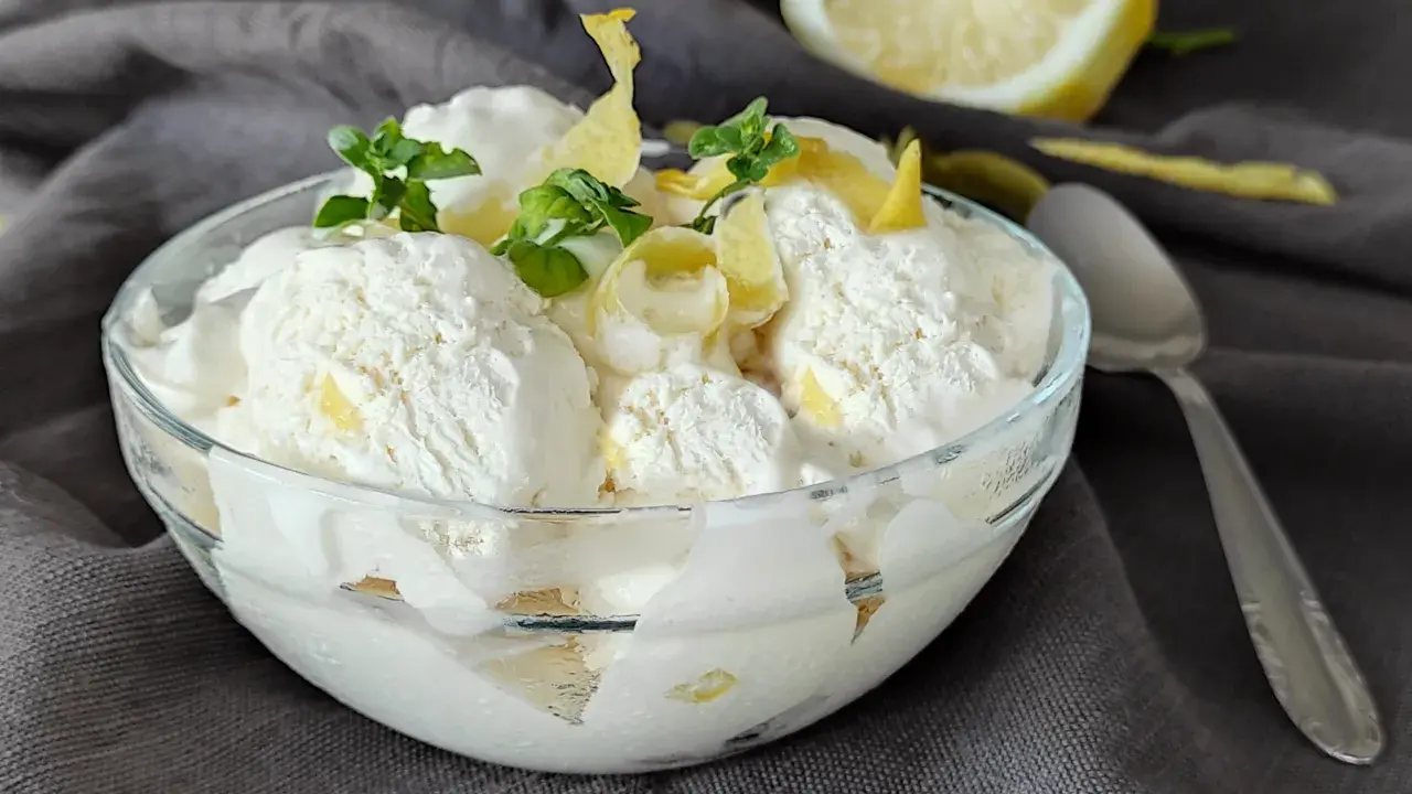 Coppa di cremoso gelato al limone, guarnita con scorzette e foglioline di menta. Un limone fresco sullo sfondo.