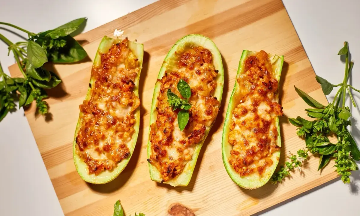 Zucchine ripiene velocissime, dorate e filanti, su tagliere di legno con basilico fresco.