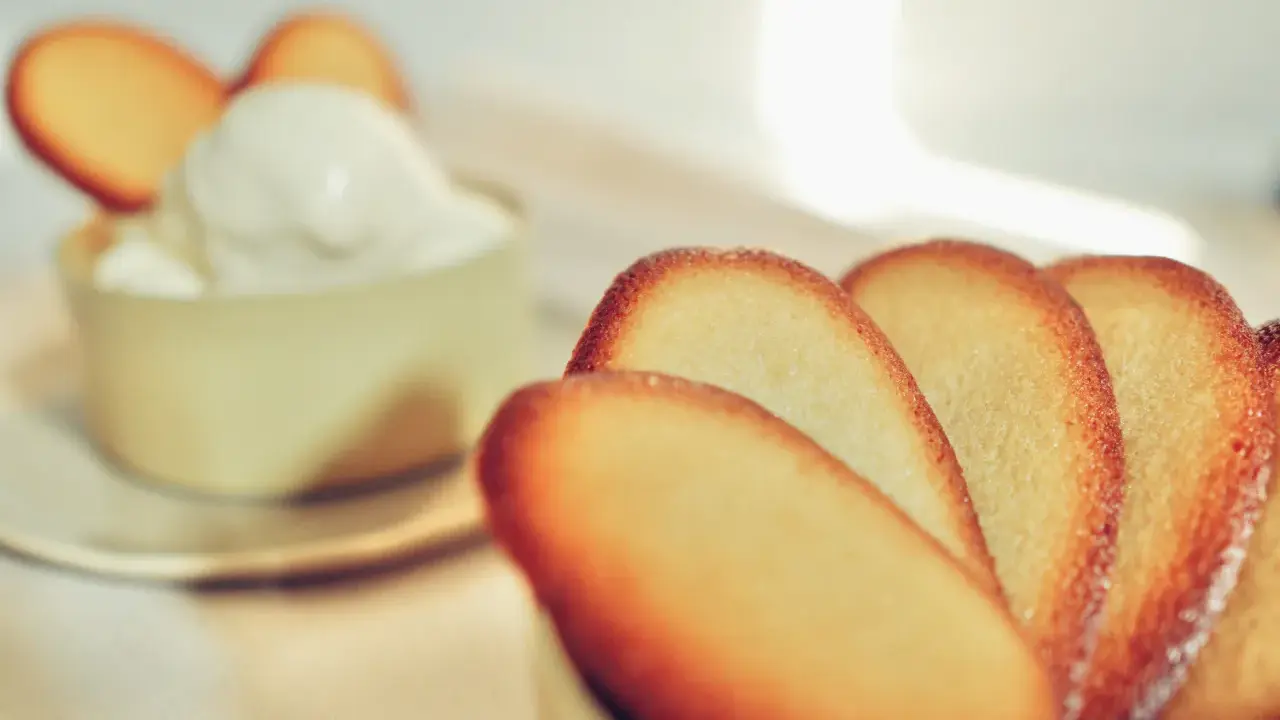 Biscotti croccanti a forma di lingue di gatto, alcuni in primo piano, altri decorano una coppa di panna montata.