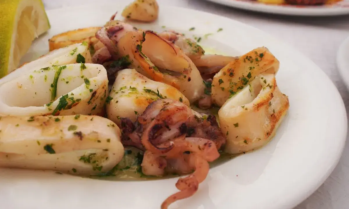 Calamari in padella, succulenti e dorati, conditi con prezzemolo fresco e serviti con una fetta di limone.