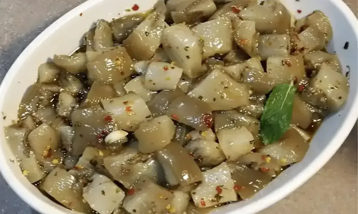 Un invitante piatto di insalata di melanzane, condita con olio, aglio e peperoncino, guarnita con una fogliolina di menta.