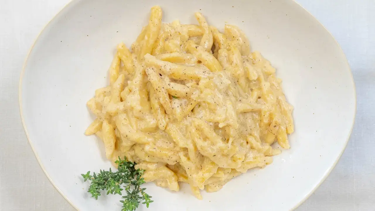 Ravioles val Varaita, pasta fresca condita con una cremosa salsa al formaggio e pepe nero, guarnita con timo fresco.
