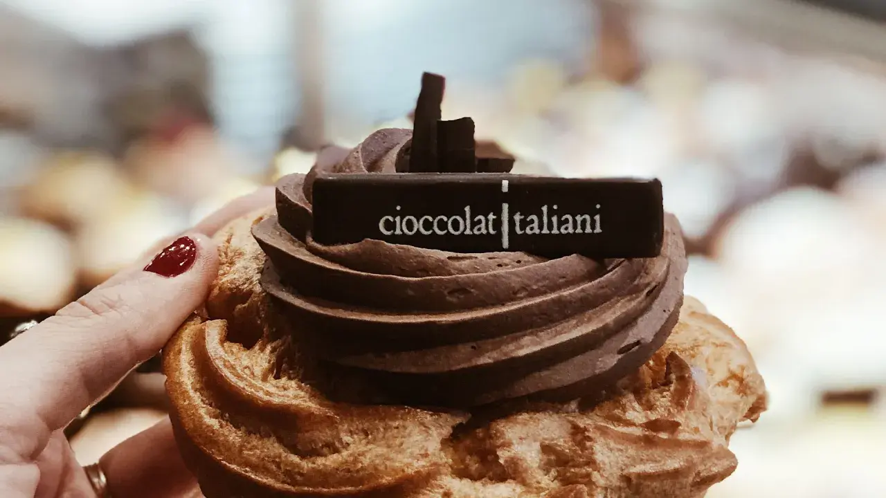 Una mano con smalto rosso tiene un delizioso dolce al cioccolato, decorato con la scritta "cioccolatitaliani".