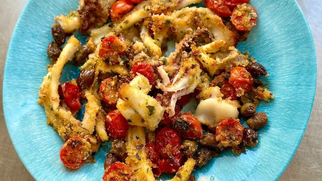 Calamari gratinati al forno su piatto blu, con pomodorini e olive. Croccanti e saporiti, un piatto che profuma di mare.