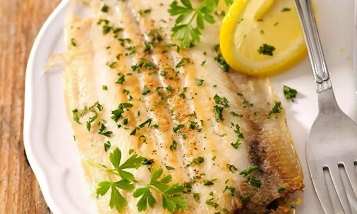 Sogliola al forno, dorata e profumata, guarnita con prezzemolo fresco e spicchi di limone. Un piatto leggero e saporito.