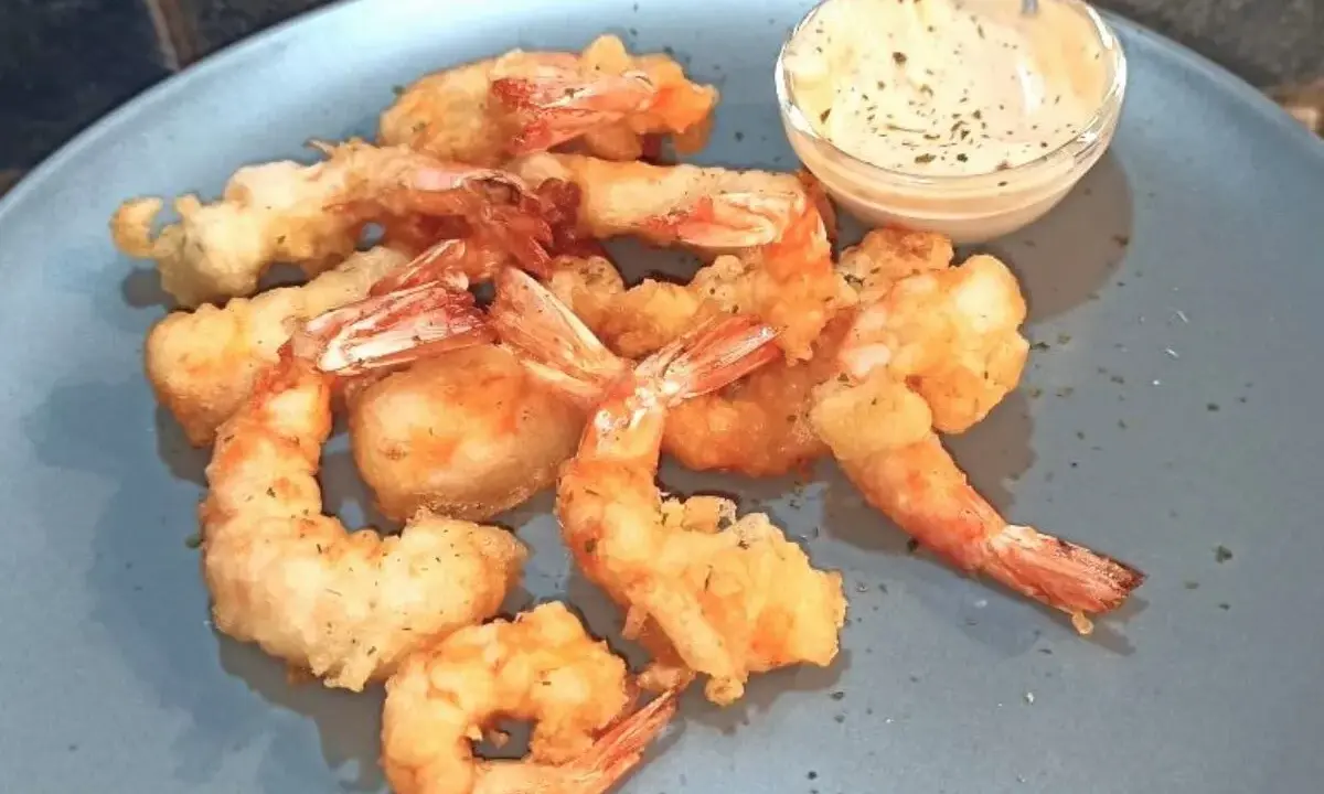 Gamberi in tempura dorati e croccanti, serviti su un piatto blu con una ciotolina di salsa cremosa.