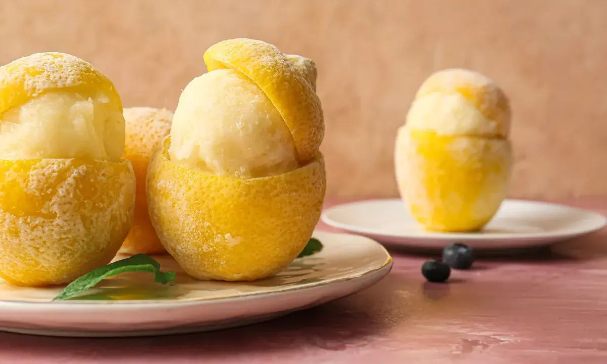 Sorbetto al limone senza albume servito in scorze di limone ghiacciate, guarnito con foglioline di menta e mirtilli.