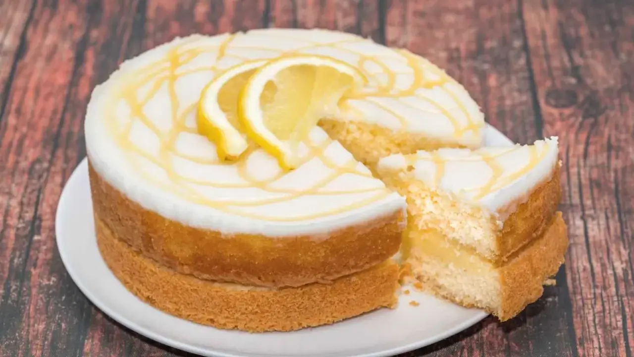Torta al limone soffice e profumata, con glassa bianca e decorazioni gialle, guarnita con fette di limone.