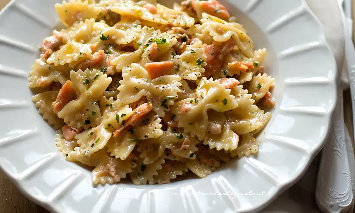 Farfalle cremose con salmone affumicato, un piatto gustoso e invitante, guarnito con prezzemolo fresco e pepe nero.