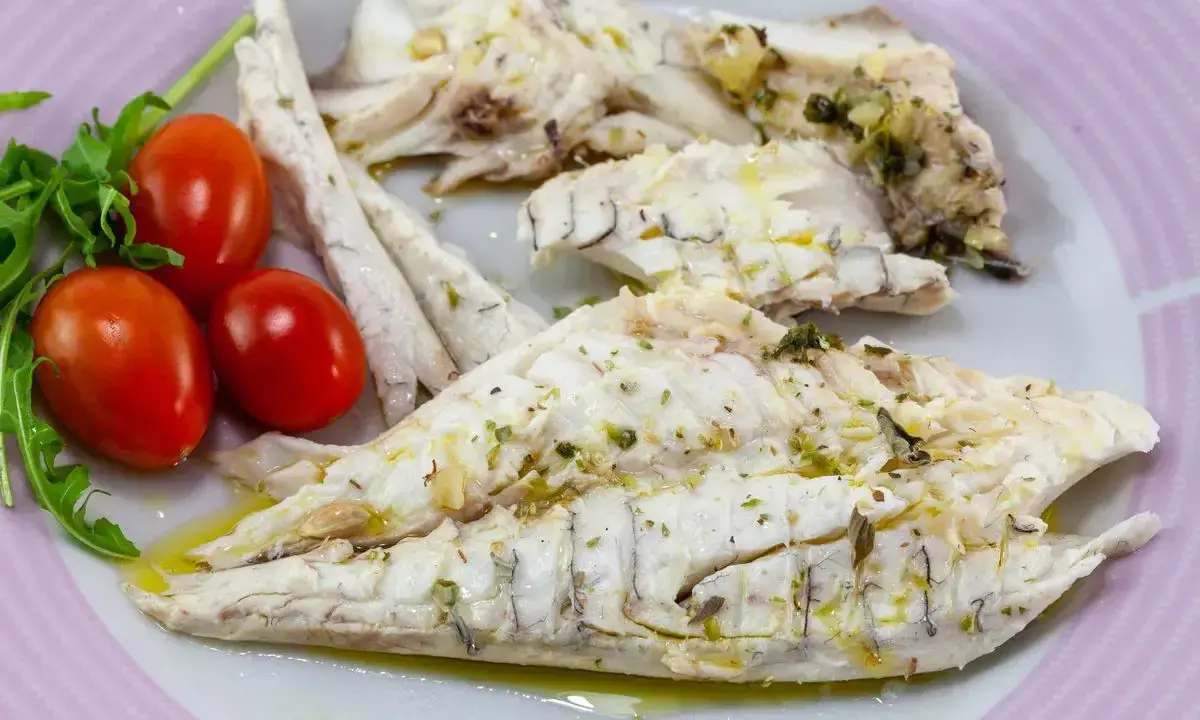 Filetti di branzino in padella, conditi con erbe aromatiche e olio d'oliva, serviti con pomodorini e rucola.