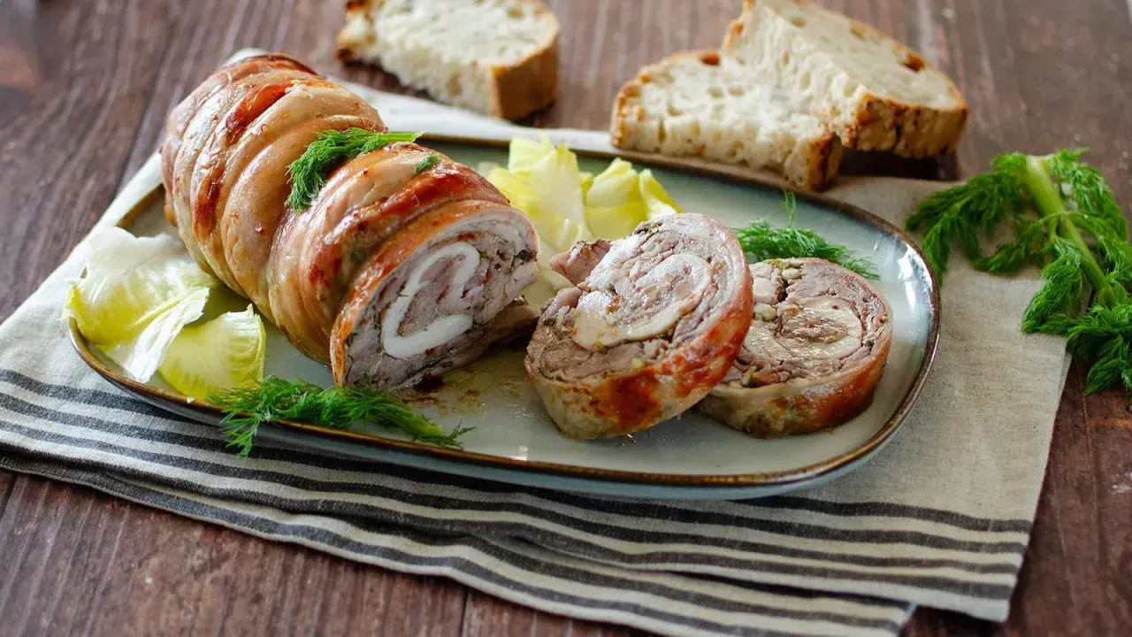 Coniglio in porchetta, un rotolo di carne succulento con erbe aromatiche, servito con pane tostato e insalata.