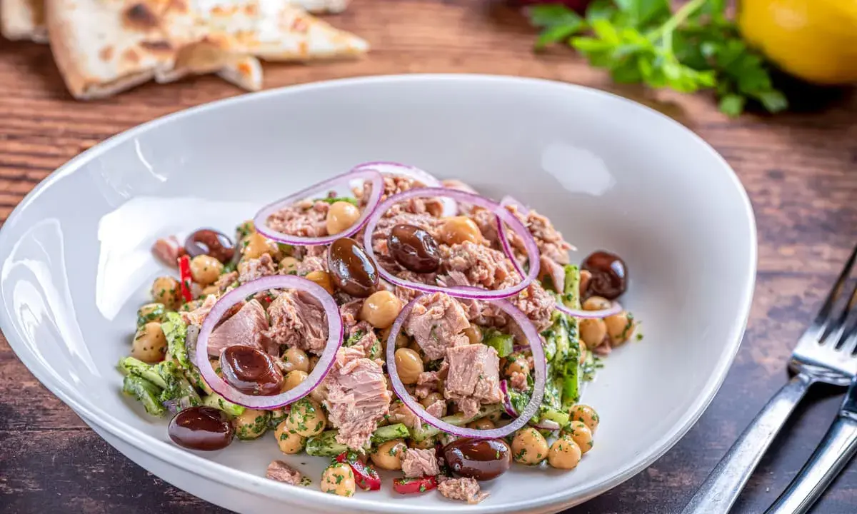 Insalata di ceci e tonno con olive nere e cipolla rossa, servita in un piatto bianco su un tavolo di legno.