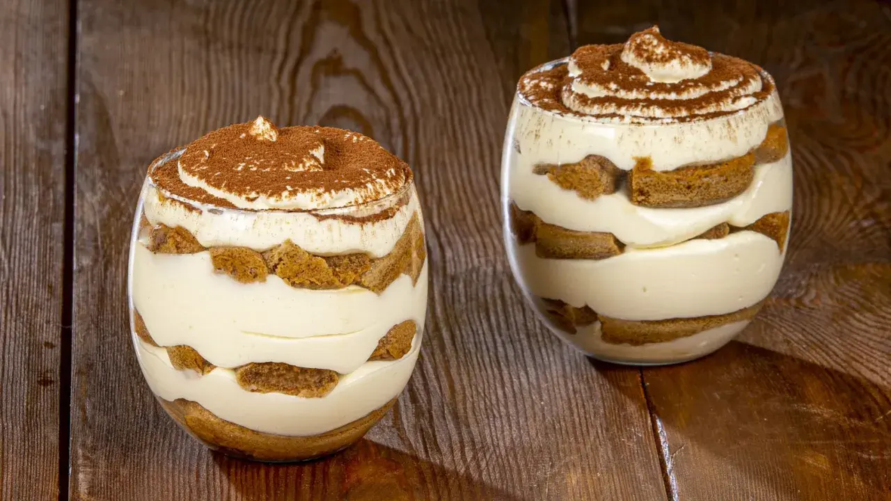 Due bicchieri di delizioso tiramisù senza uova, con strati di crema e savoiardi, spolverati di cacao.
