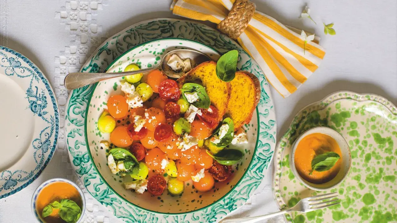 Deliziosa insalata con melone, pomodorini, formaggio e basilico, servita con pane tostato e una ciotolina di gazpacho.