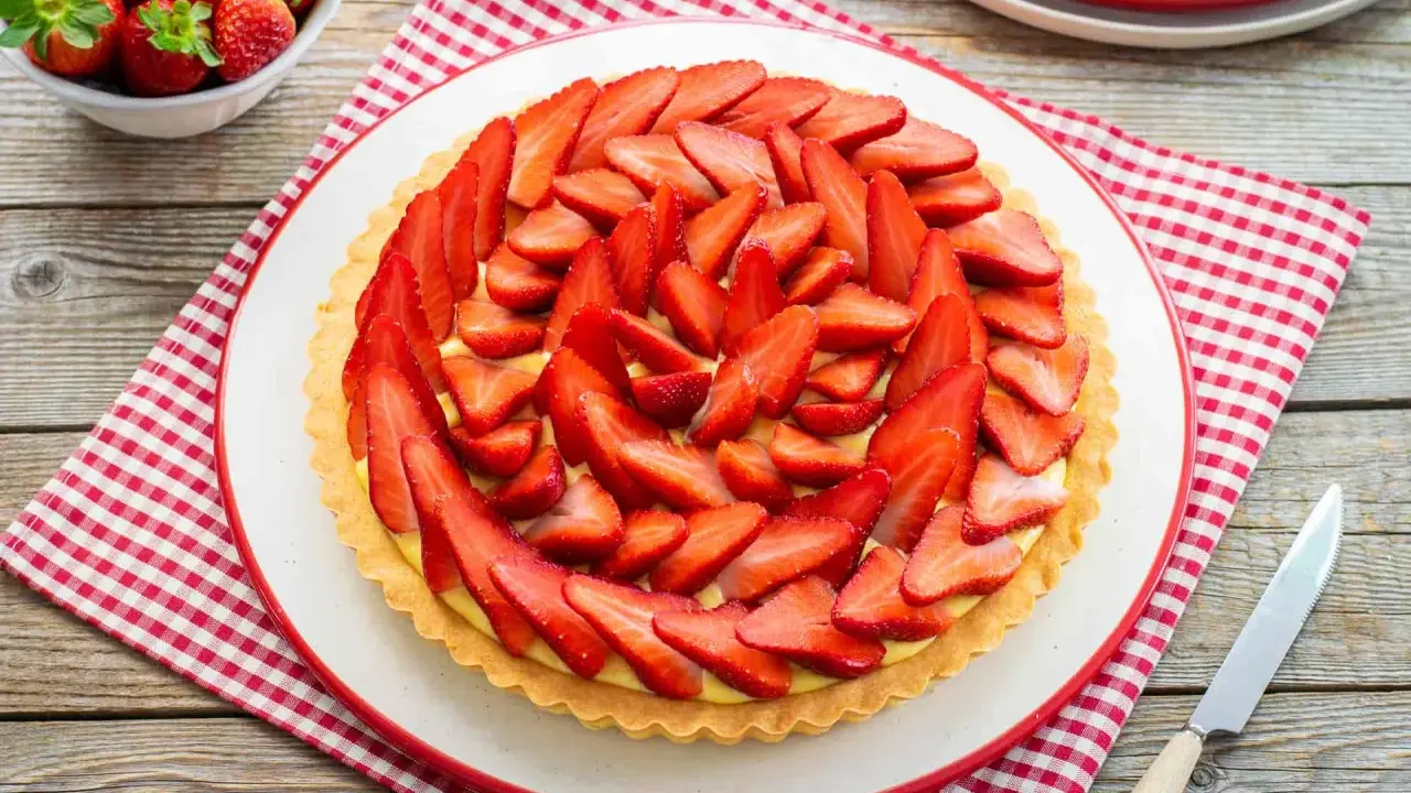 Deliziosa crostata di fragole con crema pasticcera, decorata con fragole fresche affettate. Un dolce estivo perfetto.