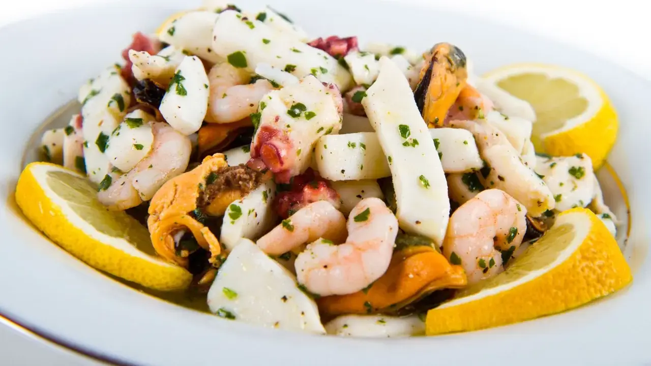 Deliziosa insalata di mare con verdure, gamberi, calamari, polpo e cozze, guarnita con spicchi di limone fresco e prezzemolo tritato.