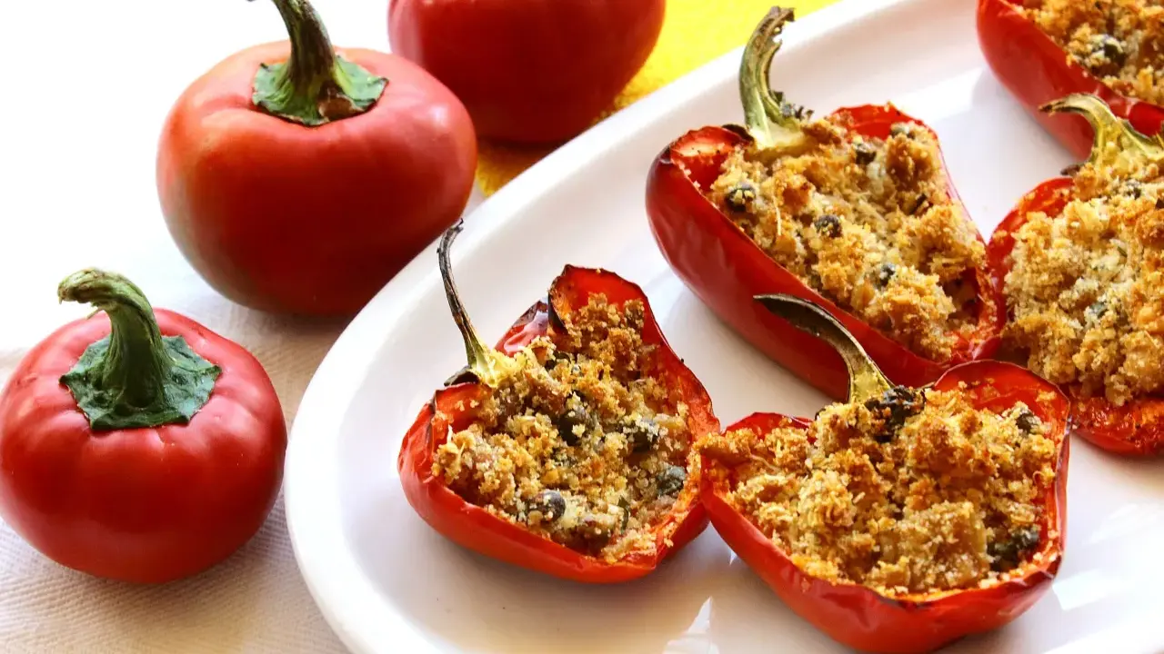 Peperoni ripieni di tonno e pangrattato, dorati e invitanti, su un piatto bianco.