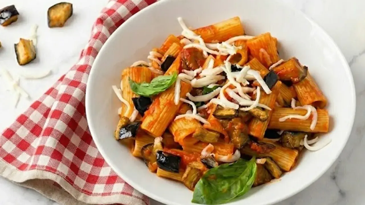 Piatto di pasta alla norma con melanzane fritte, pomodoro, basilico e ricotta salata grattugiata.