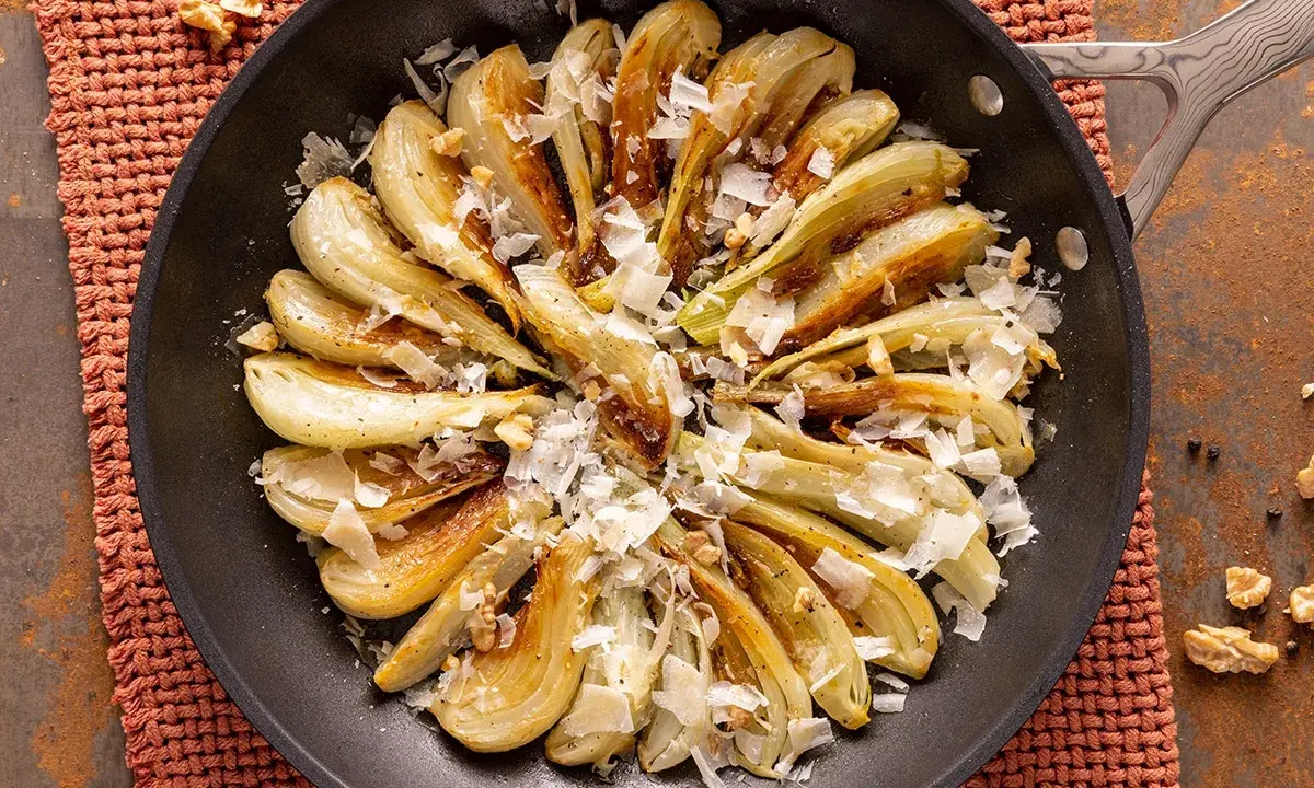 Finocchi in padella dorati, guarniti con scaglie di formaggio e noci croccanti. Un contorno saporito e invitante.