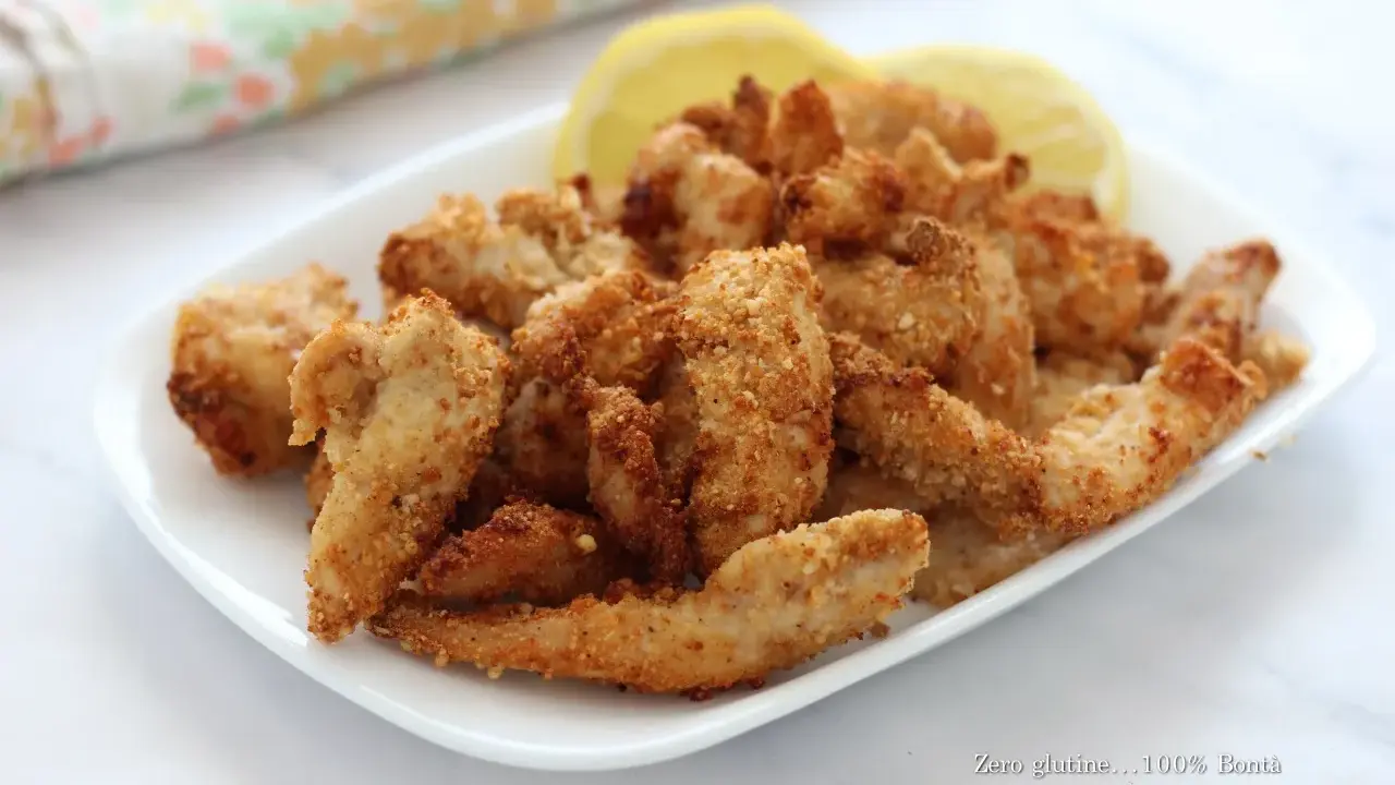 Straccetti di pollo in friggitrice ad aria, dorati e croccanti, serviti con spicchi di limone.