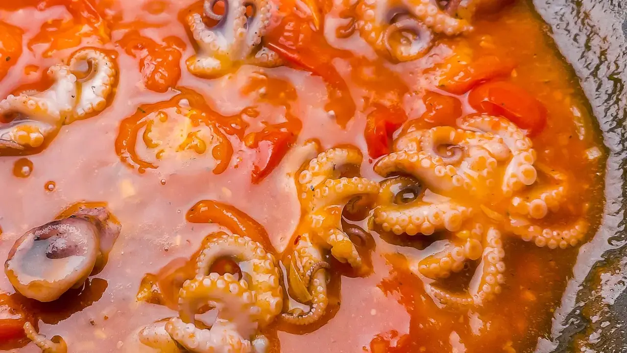 Piccolo polpo alla luciana in un sugo rosso ricco, con tentacoli visibili e pomodorini.