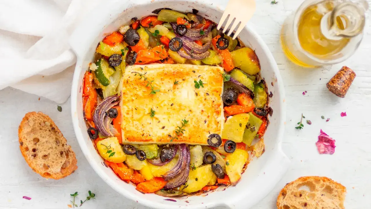 Feta al forno con verdure miste, olive nere e erbe aromatiche, accompagnata da pane rustico e olio d'oliva.