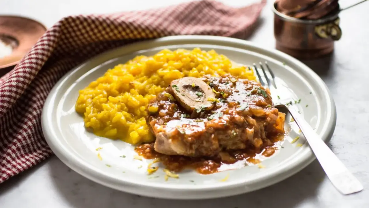 Un succulento ossobuco alla milanese, con il suo midollo invitante, adagiato su un letto di risotto giallo zafferano.