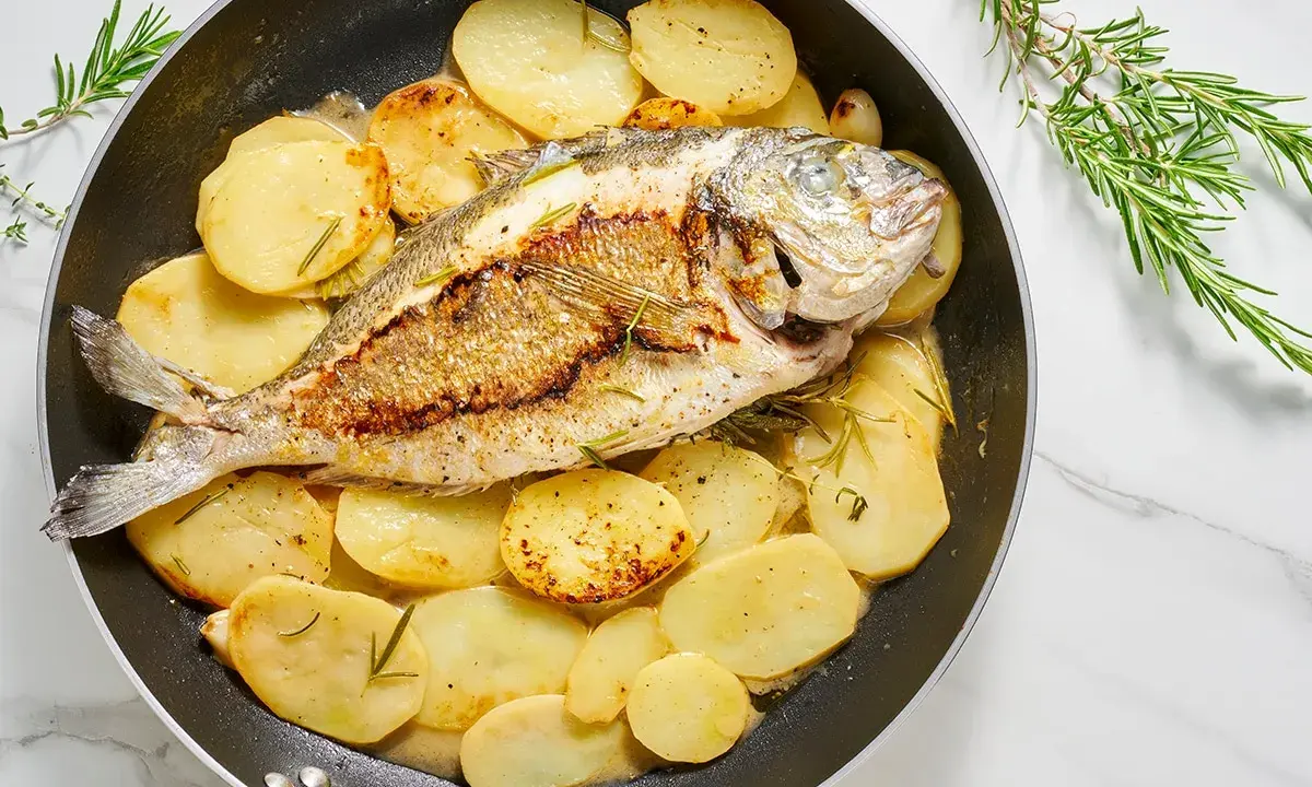 Orata in padella con patate e rosmarino, un piatto succulento e profumato, pronto per essere gustato.