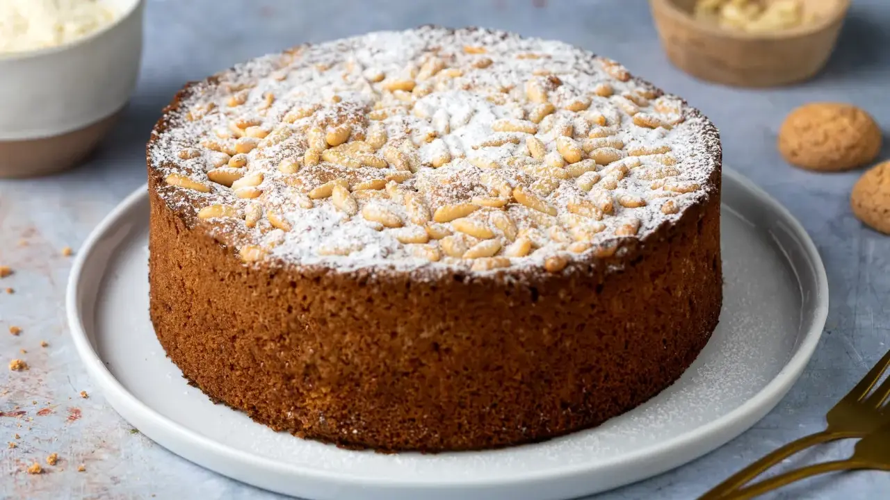 Torta soffice con farina di mandorle, guarnita con pinoli e zucchero a velo. Perfetta per ogni occasione.