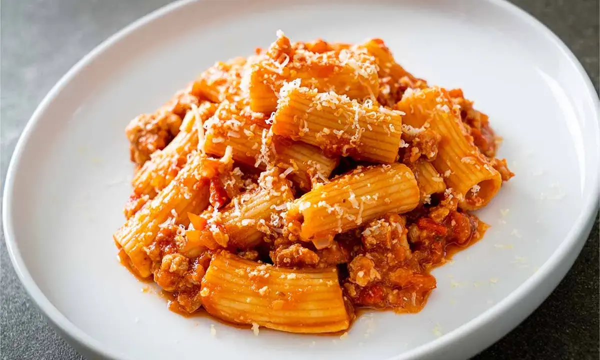 Piatto di rigatoni conditi con un ricco ragù, spolverati di parmigiano. La pasta alla zozzona ricetta perfetta per un pranzo gustoso.