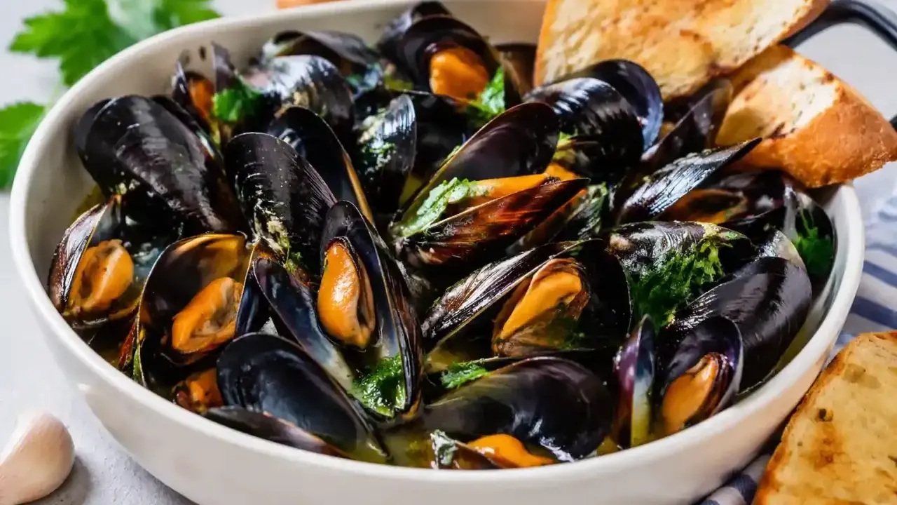 Soute di cozze fumante in una ciotola bianca, guarnita con prezzemolo fresco e accompagnata da fette di pane tostato.