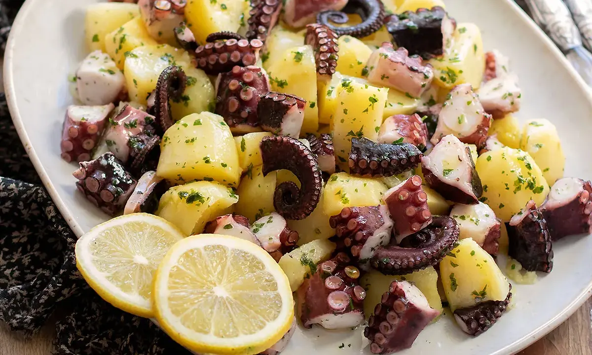 Un invitante polpo con patate, condito con prezzemolo e servito con spicchi di limone.