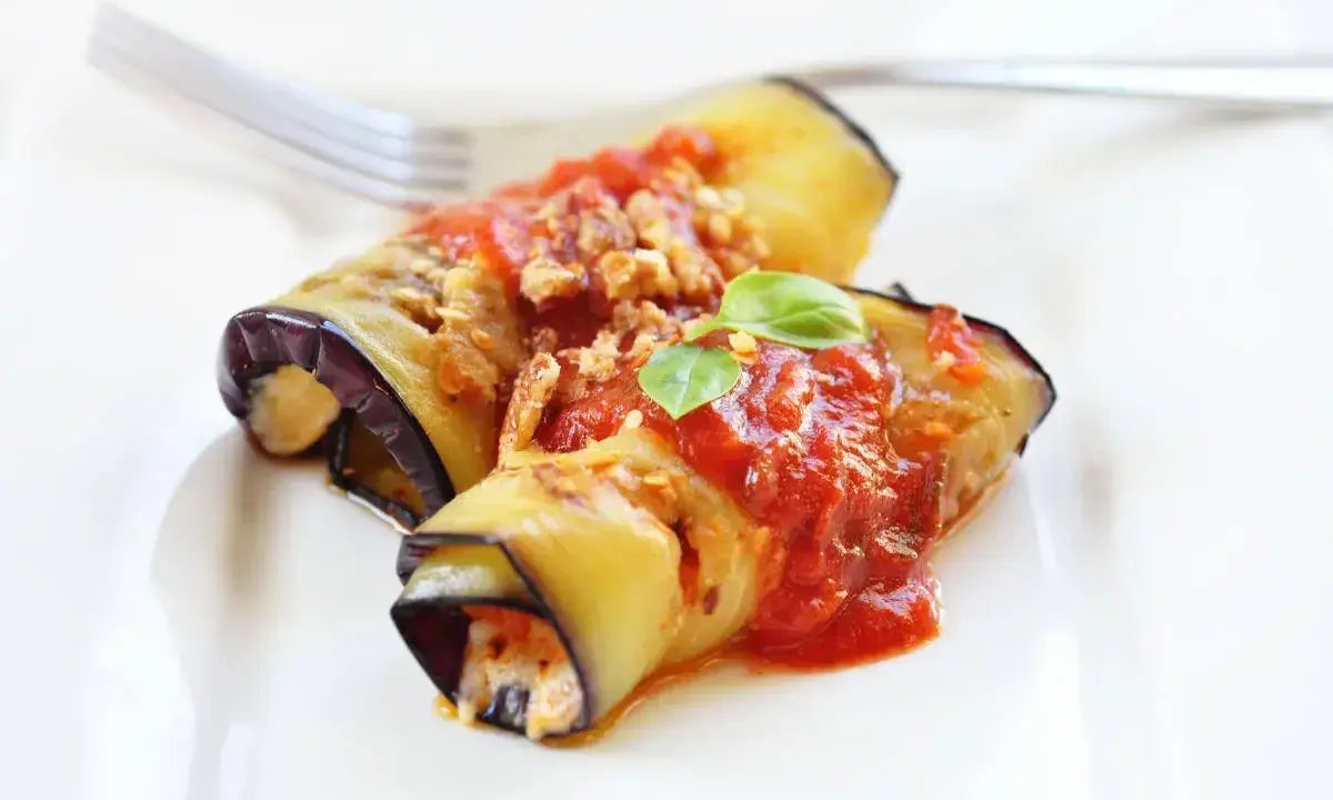 Deliziosi involtini di melanzane ripieni, conditi con sugo di pomodoro e basilico fresco, pronti per essere gustati.