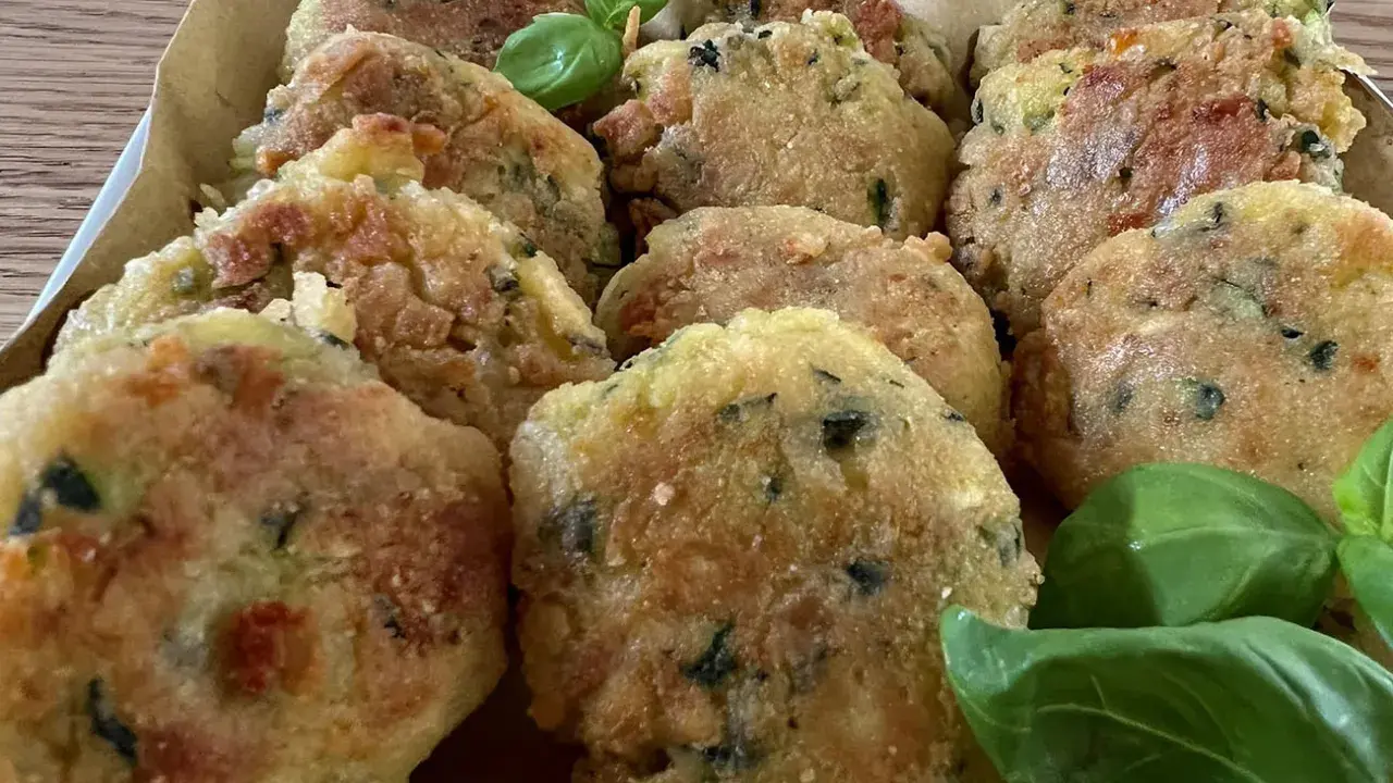 Deliziose polpette di zucchine grattugiate in padella, dorate e croccanti, guarnite con foglie di basilico fresco.