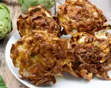 Piatto di carciofi alla giudia dorati e croccanti, con carciofi freschi sullo sfondo.