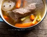 Un pezzo di carne succulenta cuoce lentamente in un brodo di carne ricco, con carote, sedano e cipolla.