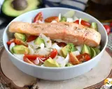 Salmone cotto su un letto di avocado, pomodorini e cipolla bianca, un piatto leggero e gustoso, perfetto come secondi di pesce.