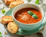 Una ciotola di cremosa zuppa di pomodoro, guarnita con basilico fresco e parmigiano, servita con crostini tostati.